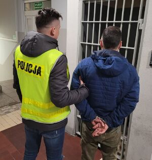 policjant prowadzi zatrzymanego po korytarzu w komendzie