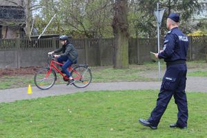 dziecko na terenie miasteczka ruchu drogowego jedzie na rowerze w kasku, policjant chodzi i ocenia jego jazdę