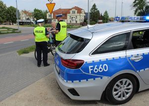 z boku stoi radiowóz, obok policjanci, którzy wręczają odblask rowerzytce