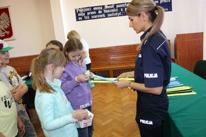 policjantka stoi w auli budynku komendy Policji w Wieluniu rozdaje dzieciom opaski odblaskowe.