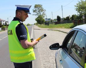 policjant trzyma w ręku alkoblow i stoi przy kontrolowanym samochodzie