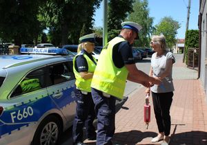 w tle radiowóz policjanci wręczają element odblaskowy pieszej