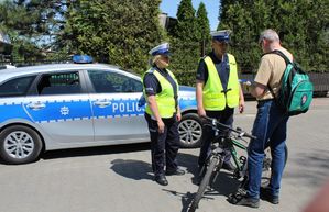 w tle radiowóz policjanci wręczają element odblaskowy rowerzyście