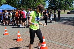 dziewczyna pokonuje slalom pomiędzy pachołkami w alkogoglach. W tle stoją uczestnicy imprezy.