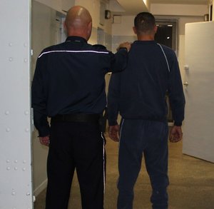zdjęcie przedstawiające policjanta prowadzącego zatrzymanego