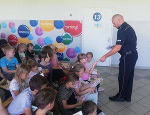 policjant rozdaje ulotki dzieciom zgromadzony w sali podczas pogadanki