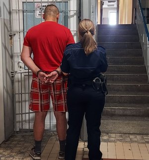 policjantka prowadzi zatrzymanego po korytarzu w budynku komendy Policji