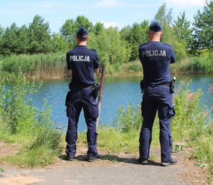 Dwóch umundurowanych policjantów stoi przy akwenie.