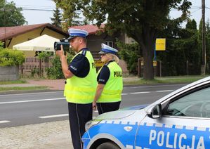 Umundurowany policjant i policjanta ruchu drogowego stoją przy radiowozie przy drodze i kontrolują prędkość przy użyciu  ręcznego miernika.