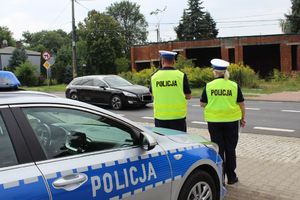 Umundurowany policjant i policjanta ruchu drogowego stoją przy radiowozie przy drodze i nadzorują ruch.