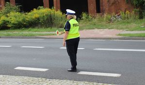 Umundurowana policjantka stoi na drodze i zatrzymuje tarczą pojazdy.