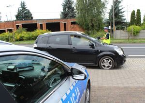 Umundurowany policjant prowadzi kontrolę drogową zatrzymanego pojazdu.