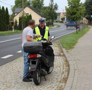Umundurowany policjant prowadzi kontrolę motocyklisty.