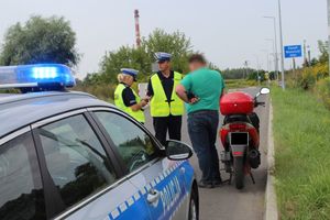 Umundurowany policjant i policjantka  prowadzą kontrolę motocyklisty.