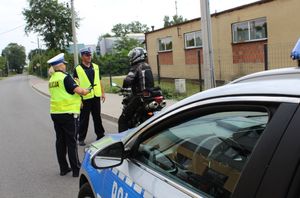 Umundurowany policjant i policjantka  prowadzą kontrolę motocyklisty.