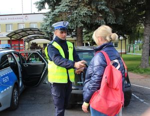 Policjant wręcza opaskę odblaskową kobiecie.