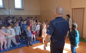 Umundurowany policjant i w sali w szkole z uczniami prowadzi pogadankę edukacyjną.