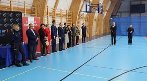 Zaproszeni goście stoją na hali sportowej, przemawia Starosta Wieluński.