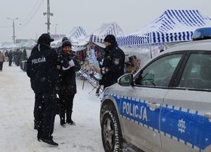 Policjanci na targowisku wręczają ulotki i elementy odblaskowe seniorom, z boku stoi radiowóz.