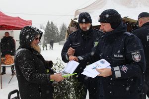 Policjanci na targowisku wręczają ulotki i elementy odblaskowe seniorom.