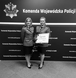 Komendant Powiatowy Policji w Wieluniu pozuje do zdjęcia z wyróżnioną dzielnicową z wieluńskiej komendy na tle baneru Komenda Wojewódzka Policji w Łodzi.