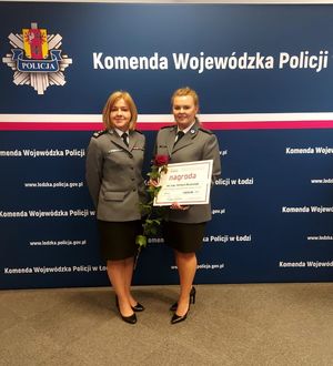 Komendant Powiatowy Policji w Wieluniu pozuje do zdjęcia z wyróżnioną dzielnicową z wieluńskiej komendy na tle baneru Komenda Wojewódzka Policji w Łodzi.