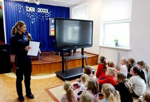 Policjantka w szkole w sali prowadzi pogadankę z dziećmi, które siedzą naprzeciwko.