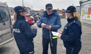 Policjantki wręczają odblask i ulotkę mężczyźnie.