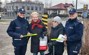 Dwie umundurowane policjantki rozdają na mieście ulotki i odblaski, pozują do zdjęcia z dwoma seniorkami.