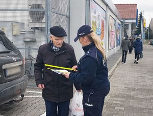 Policjantka wręcza odblask i ulotkę mężczyźnie.