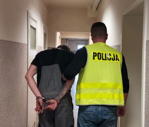 Policjant prowadzi zatrzymanego po korytarzu w budynku komendy.