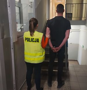 Policjantka prowadzi zatrzymanego po korytarzu w budynku komendy.