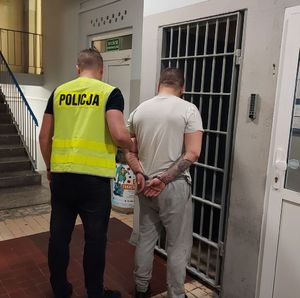 Policjant prowadzi zatrzymanego po korytarzu w budynku komendy.