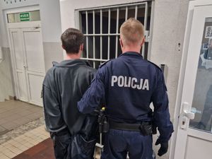 Policjant prowadzi zatrzymanego po korytarzu w budynku komendy.