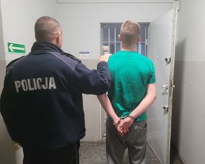 Policjant prowadzi zatrzymanego po korytarzu do pomieszczenia dla osób zatrzymanych w budynku wieluńskiej komendy.