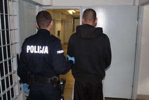 Policjant umundurowany prowadzi zatrzymanego po korytarzu w budynku komendy.