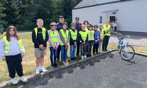 Dzieci ubrane w kamizelki odblaskowe pozują wspólnie z dzielnicowymi do zdjęcia.