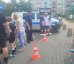 Stoisko profilaktyczne wystawione przez policjantów z wieluńskiej komendy na turnieju charytatywnym. Mężczyzna pokonuje tor przeszkód w alkogoglach obok stoi policjant.