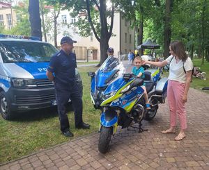 Dziecko siedzi na motocyklu, obok policjant w tle radiowóz.