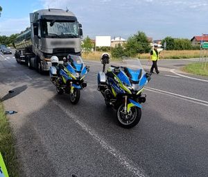 Motocykle policyjne oraz ciężarówka uczestnicząca w wypadku drogowym, z boku idzie policjant.