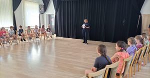 Policjantka stoi w sali, wokół siedzą dzieci i słuchają pogadanki.