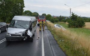 Miejsce wypadku, rozbity bus stojący na drodze uczestniczący w zdarzeniu, dalej poza drogą rozbity samochód osobowy, w tle pracujące służby ratunkowe.
