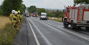 Miejsce wypadku, rozbity bus stojący na drodze uczestniczący w zdarzeniu, dalej  poza drogą rozbity samochód osobowy, w tle pracujące służby ratunkowe.