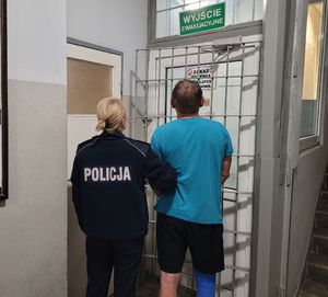 Policjantka prowadzi zatrzymanego po korytarzu w budynku komendy.