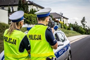 Policjanci na drodze mierzą prędkość Obok stoi radiowóz.