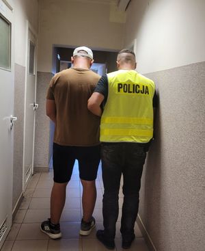 Policjant prowadzi zatrzymanego po korytarzu w budynku komendy policji.