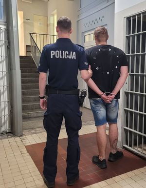 Policjant prowadzi zatrzymanego po korytarzu w budynku komendy.