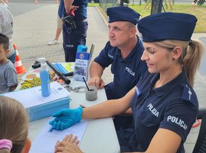 Policjantka  i policjant podczas pikniku robią  pamiątkowe odbitki linii papilarnych.