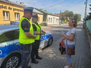 Policjanci wręczają pieszej element odblaskowy.