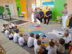 W sali przedszkolnej policjanci prowadzą pogadankę z dziećmi.